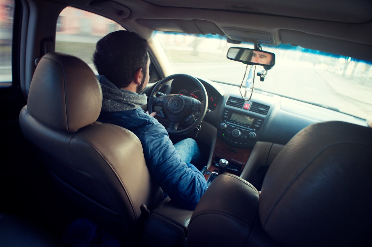 about-us A man driving a car with focus on interior, dashboard, and steering wheel, captured from the backseat.